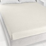 Prześcieradło żakardowe bez gumki w kolorze ecru o wymiarach 175x220 cm, rozłożone na łóżku. Wzór żakardowy z delikatnymi zdobieniami, materiał matowy, dobrze dopasowane do krawędzi materaca. Widoczne białe poduszki w tle.