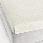 Prześcieradło żakardowe bez gumki 175x220 w kolorze ecru, rozłożone na łóżku, o delikatnym wzorze teksturalnym, oferujące elegancki wygląd. Widać je w górnej części, z krawędzią lekko opadającą na materac, na jednolitym tle.