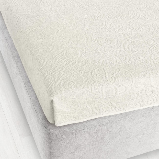 Prześcieradło żakardowe bez gumki 175x220 w kolorze ecru, rozłożone na łóżku, o delikatnym wzorze teksturalnym, oferujące elegancki wygląd. Widać je w górnej części, z krawędzią lekko opadającą na materac, na jednolitym tle.