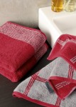 Ręcznik bawełniany 80x150 w kolorze krwistej czerwieni z szarym wzorem kraty, leżący na ciemnym blacie. W zasięgu wzroku znajduje się logo na etykiecie oraz dwa butelki z kosmetykami. W tle widoczna szara ściana.