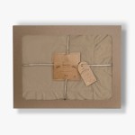 Pościel bawełniana z falbanką 220x200 w kolorze beżowym, opakowana w kartonowe pudełko z przezroczystą szybą. Widoczne metki z nazwą marki LIMASSO oraz informacjami o produkcie. Zestaw wiązany naturalnym sznurkiem.