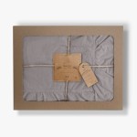 Pościel bawełniana z falbanką w kolorze szarym, rozmiar 220x200 cm, zapakowana w kartonowe pudełko z transparentnym oknem. Użyta naturalna bawełna, z widoczną etykietą oraz dekoracyjnym sznurkiem. Falbanka na dolnej krawędzi otrzymała mocne wykończenie.