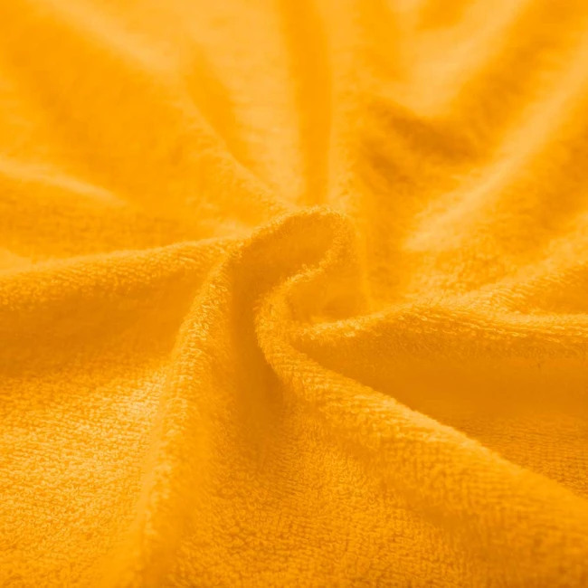 Prześcieradło frotte z gumką w kolorze żółtym, wykonane z miękkiego materiału o teksturze pętelkowej, leży na powierzchni. Idealne do łóżeczka o wymiarach 40x90 cm. Zbliżenie na fakturę materiału, ukazujące jego grubość i wygodę użytkowania.