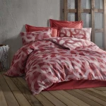 Pościel bawełniana 160x200 w kolorze terakoty z wzorem w stylu jacquard z okręgami, leżąca na łóżku. Na zdjęciu widoczne poduszki w tym samym kolorze, ułożone w sposób swobodny. Tło w odcieniach szarości, naturalne drewno podłogi, atmosfera przytulności.