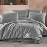 Pościel satyna bawełniana 180x200 w kolorze szarym, z delikatnym, wzorzystym splotem. Zestaw zawiera poszwę na kołdrę i poduszki, układany na łóżku w stylowej aranżacji, z gładką fakturą materiału.
