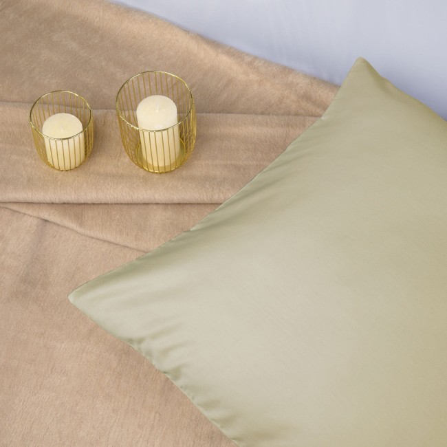 Poszewka satynowa 70x80 w kolorze kremowym, leżąca na jasnym tle. Widoczna gładka faktura materiału, bez wzorów. Obok stoją dwa świeczniki z żółtymi świecami. Tło proste, minimalne, skupione na produkcie.