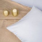 Poszewka satynowa 70x80 cm w kolorze białym, leżąca na jasnym tle. Produkt ma gładką, błyszczącą fakturę. Obok znajdują się dwie świeczki umieszczone w złotych, drucianych holderach.