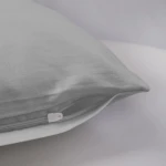 Pościel satyna bawełniana 140x200 w kolorze popielatym, z zamkiem błyskawicznym. Ujęcie z boku, ukazujące gładką fakturę i detal zamka. Produkt leży na jasnym tle, co podkreśla jego kolorystykę i elegancki materiał.