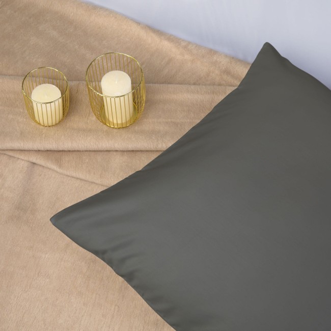 Pościel satyna bawełniana 220x200 w kolorze szarym, rozłożona na jasnym tle. Na poduszce widoczna gładka faktura materiału. Obok dwa świeczniki z drucianymi osłonami oraz białe świeczki.