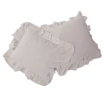 Pościel bawełniana w kolorze naturalnej kremowej, rozmiar 160x200 cm, z falbanką. Złożona poduszka i poszwa na kołdrę z widoczną teksturą materiału, leżące na białym tle. Falbanka zdobi krawędzie poduszek.