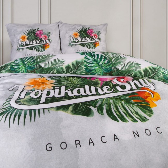 Pościel bawełniana 220x200, wzór tropikalny, z nadrukiem zielonych liści i kolorowych kwiatów na jasnoszarym tle. Zestaw zawiera poszewki na poduszki z napisem Tropikalne Sny. Produkt leżący na łóżku, z bliska prezentujący detale wzoru oraz tekst.