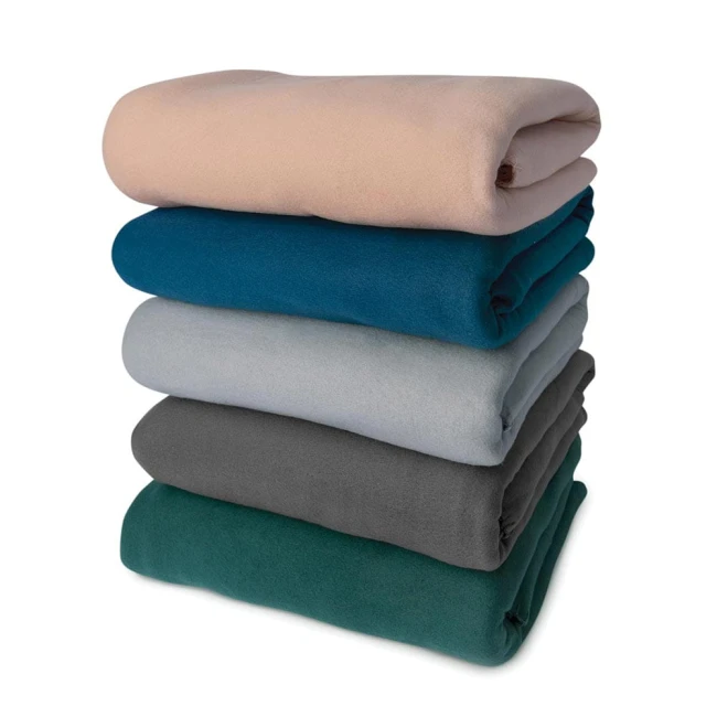 Koc polarowy Lukka 150x200 cm w kolorze butelkowej zieleni, złożony i umieszczony na górze stosu wśród innych koców. Widać gładką teksturę materiału oraz solidne wykończenie. Tło proste, białe.