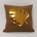 Poszewka dekoracyjna 40x40 cm w odcieniu brązowym z efektownym, złotym liściem. Wzór liścia jest wycięty z materiału, co nadaje trójwymiarowy efekt. Produkt leży na jednolitym tle, prezentując matową fakturę tkaniny.