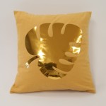 Poszewka dekoracyjna 40x40 cm w kolorze złotym z liściem monstery w powierzchni błyszczącej. Produkt leży na gładkim tle, a kształt liścia jest wycięty w materiale, podkreślając fakturę i kolor tkaniny.