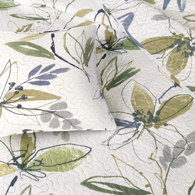 Narzuta drukowana Flori 170x210 w kolorze białym z zielonymi, niebieskimi i szarymi wzorami roślinnymi, delikatnie pikowana. Położona na łóżku z poduszką, widoczna faktura materiału. Produkt rozłożony w perspektywie z góry.