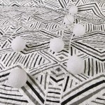 Narzuta drukowana Tarik 170x210 w biało-czarnym geometrycznym wzorze, leżąca na jasnym tle. Widoczne dekoracyjne kulki z białego materiału, rozłożone wzdłuż narzuty, dodające efektu stylowego wystroju. Idealna do nowoczesnych aranżacji wnętrz.