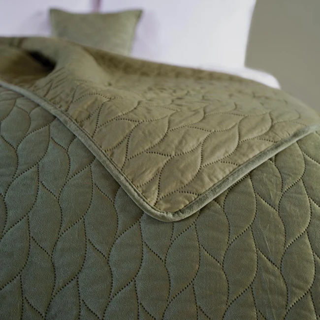 Narzuta Verde mink w kolorze zielonym, o wymiarach 240x220 cm, z delikatnym, falistym wzorem i matową fakturą. Ułożona na łóżku, z widocznym poduszką w tym samym kolorze, prezentuje elegancki styl.