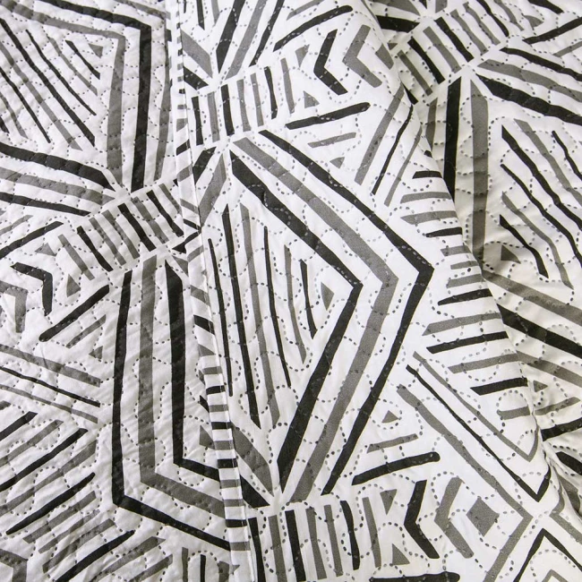 Poszewka na poduszkę 40x40 cm, wykonana z materiału w biało-czarnym wzorze geometrycznym. Ujęcie zbliżeniowe, ukazujące detale faktury tkaniny. Poszewka leży na płaskiej powierzchni, bez widocznych napisów czy logo.