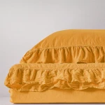 Pościel bawełniana z falbanką w kolorze żółtym o wymiarach 160x200, leżąca na jednolitym tle. Materiał ma gładką fakturę, a falbanek dodaje dekoracyjny akcent. Widoczna jest poduszka oraz nakładka na kołdrę, ujęcie z boku.