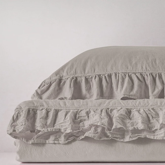 Pościel bawełniana z falbanką 220x200 w odcieniu naturalnej kremowej, leżąca na gładkiej powierzchni. Widoczny detal falbanki oraz tekstura materiału. Produkt rozłożony, ukazujący miękkość i elegancki fason. Tło jasne, jednolite.