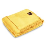 Koc bawełniany, rozłożony w kolorze intensywnego żółtego, o wymiarach 150x200 cm. Z widocznymi frędzlami na krótszym boku oraz delikatną teksturą. Ujęcie z boku, na białym tle, pokazuje jego złożony kształt oraz stylowe wykończenie.