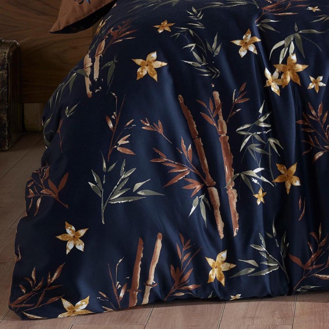 Pościel satyna bawełniana 160x200 z motywem kwiatów i bambusa. Tło w ciemnym odcieniu granatu z delikatnymi, złotymi i zielonymi detalami. Widoczny fragment poszwy, leżącej na drewnianej podłodze, z eleganckimi roślinnymi wzorami.