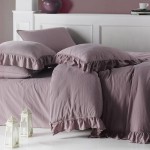 Komplet dwóch poszewek bawełnianych 40x40 cm w odcieniu fioletowym, z dekoracyjną falbanką. Ułożone na łóżku, z widoczną teksturą materiału. W tle biały parawan i subtelne detale aranżacyjne, takie jak lampiony.