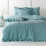 Komplet poszewek bawełnianych z falbanką 2x40x40 cm w kolorze mineralnym niebieskim. Widok z przodu, poszewki leżą płasko na łóżku, falbanka wykończenia i miękka tekstura tkaniny są dobrze widoczne, w otoczeniu minimalistycznym białym tle.