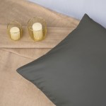 Poszewka satynowa 50x70 w kolorze szarym, leżąca na tle jasnego materiału. Z boku dwie świeczki w złotej osłonie. Gładka, błyszcząca faktura poszewki podkreślająca elegancję. Brak widocznych napisów lub logo.