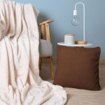 Poszewka żakardowa 40x40 w kolorze mlecznej czekolady, z fakturą wzdłużnych żłobień, leżąca na stoliku obok zasłony z miękkiego materiału. Produkt umieszczony w nowoczesnym wnętrzu, na tle jasnoniebieskiej ściany.