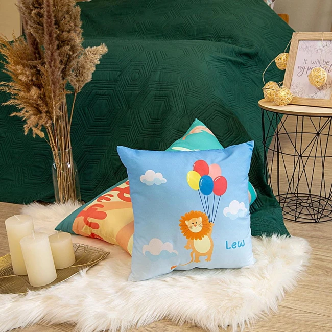 Poduszka przytulanka w kształcie lwa, rozmiar 40x40 cm, z jasnoniebieską tkaniną, zdobiona kolorowym nadrukiem lwa trzymającego balony. Produkt leży na białym, futrzanym tle obok innych poduszek w złożonej aranżacji na podłodze.