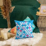 Poduszka przytulanka w kształcie ryby, rozmiar 40x40 cm, w kolorze błękitnym z wzorem w białe, różowe i niebieskie łuski. Produkt leży na białym futrze, obok kilku innych poduszek. W tle zielony koc oraz dekoracyjny stół z świecami i ozdobami.