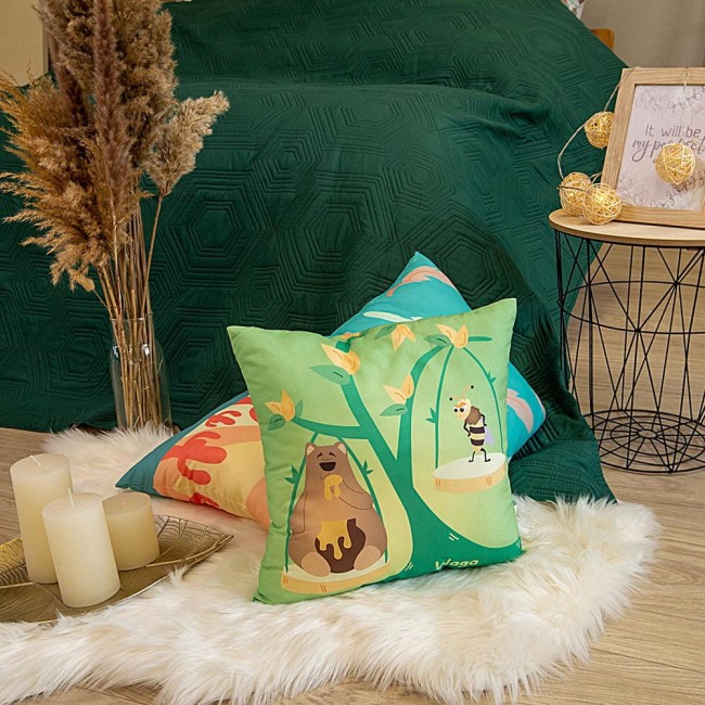 Poduszka przytulanka Waga 40x40 w kolorze zielonym, z rysunkami niedźwiedzia i pszczoły na tle natury. Ułożona na pufie z futrzanym podkładem, z widocznymi dekoracyjnymi elementami. Zbliżenie na detale użytku w aranżacji wnętrza.