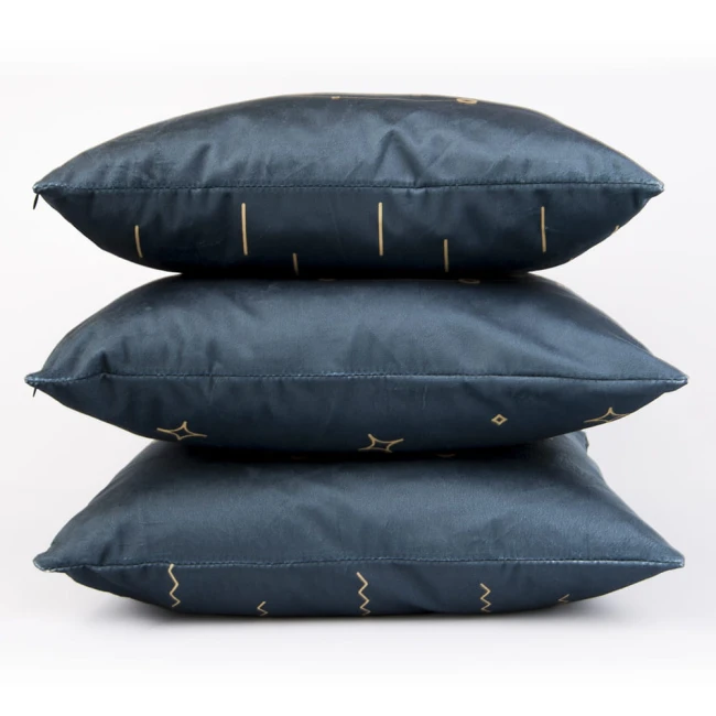 Poszewka dekoracyjna 40x40 w granatowym kolorze z złotymi wzorami, ułożona w stosie. Materiał satynowy, matowy, z widocznymi geometrycznymi kształtami, takimi jak linie i gwiazdki. Produkt leży na białym tle.