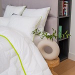 Poduszka antyalergiczna pikowana 50x60 cm w białym kolorze z zielonym obszyciem leży na pościeli. W tle widoczne trzy poduszki na wezgłowiu łóżka oraz ozdobny element w kształcie pierścienia z liśćmi na stoliku.