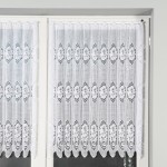 Biała żakardowa zazdrostka o wymiarach 120 cm, zawieszona na karniszu. Wyraźny wzór z floralnymi motywami w odcieniach bieli, zygzakowate wykończenie dolnej krawędzi.