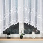 Firana żakardowa Bakaro w kolorze białym, o wymiarach 520x160 cm, zawieszona na oknie. Materiał gładki z haftowanym wzorem roślinnym na dolnej krawędzi. W tle dwa lampiony i doniczka z orchideą na parapecie.
