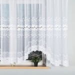 Firana gotowa Bastia żakardowa biała 500x160 z delikatnym wzorem liści i kwiatów na dolnej krawędzi. Produkt zawieszony na oknie, lekko zwisający, wykonany z transparentnego materiału. Widoczna doniczka z zieloną rośliną na parapecie.