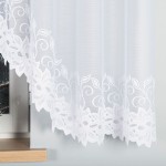 Firana gotowa Bastia w kolorze białym, wykonana z żakardowego materiału, wisząca, z delikatnym, koronkowym wykończeniem na dole. Produkt umieszczony przy oknie, na tle ciemniejszego otoczenia. Wymiary: 500x160 cm.
