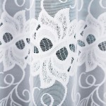 Firana żakardowa, biała, o wymiarach 500x160 cm, z delikatnym kwiatowym wzorem. Ujęcie z bliska, widać szczegóły faktury tkaniny. Tło jest proste, co podkreśla wzór firany. Produkt jest zwisający, zachowując lekkość i elegancję.