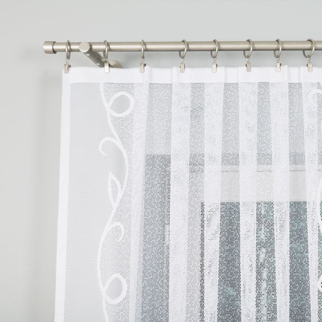Firana żakardowa w kolorze białym, o wymiarach 300x160 cm, w delikatny wzór z motywem roślinnym. Zawieszona na metalowej karniszu, widoczna z bliska, ukazująca teksturę tkaniny. Tło jasne, neutralne, co podkreśla elegancję firany.