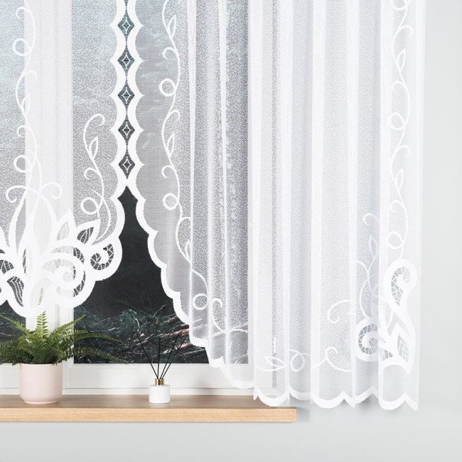 Firana żakardowa w kolorze białym, o wymiarach 400x160 cm, z dekoracyjnym wzorem w formie falistej bordiury. Produkt prezentowany na białym tle, wiszący na oknie, obok doniczka z rośliną i świecznikiem. Ujęcie z boku.