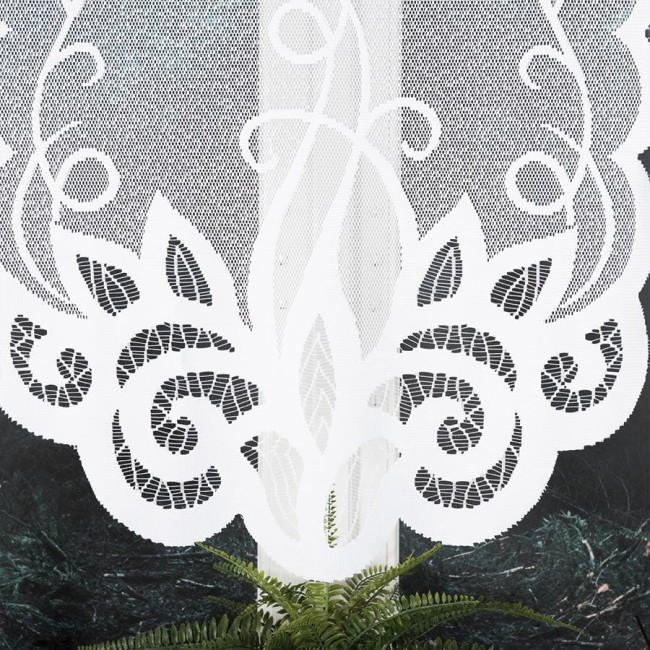 Firana gotowa Ewelina żakardowa w kolorze białym, o wymiarach 400x160 cm. Produkt ozdobiony delikatnym, ażurowym wzorem roślinnym. Zawieszona w poziomie, na jednolitym tle. Wyraźne detale wzoru podkreślają teksturę materiału. Roślina doniczkowa w tle.