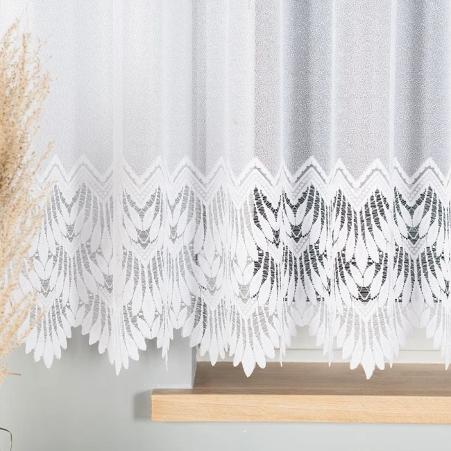 Firana gotowa Felicja żakardowa, biała, o wymiarach 400x160 cm. Produkt wiszący, widoczny na frontalnym zbliżeniu, z dekoracyjnym wzorem w liście na dolnej krawędzi. Tło proste, w odcieniach szarości, z naturalnym elementem trawy.