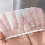 Firana żakardowa z ołowianką w kolorze białym, wysokość 250 cm, o delikatnym wzorze. Ujęcie z góry, na tle neutralnym, prezentująca fakturę siateczki. Widoczna biała krawędź z ozdobnym wykończeniem. Produkt trzymany w dłoniach.