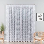 Firana żakardowa Zuzanna w białym kolorze o wysokości 250 cm, z delikatnym wzorem roślinnym. Produkt wiszący, ujęcie frontalne. Tło w stonowanym odcieniu szarości, w otoczeniu stylowego zestawu mebli. Detale haftu na firanie dobrze widoczne.