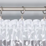 Firana żakardowa Zuzanna w kolorze białym, o wysokości 250 cm, z delikatnym wzorem roślinnym. Wisząca na metalowej karniszu, ukazuje falbany oraz subtelną teksturę materiału. Tło jest jednolite i jasne, co podkreśla elegancję firany.