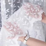 Firana żakardowa Zuzanna w kolorze białym, wysokość 250 cm, z delikatnym wzorem liści. Produkt rozłożony, uchwycony w zbliżeniu na detale, z widoczną koronkową krawędzią. Tło simple, co podkreśla fakturę materiału.