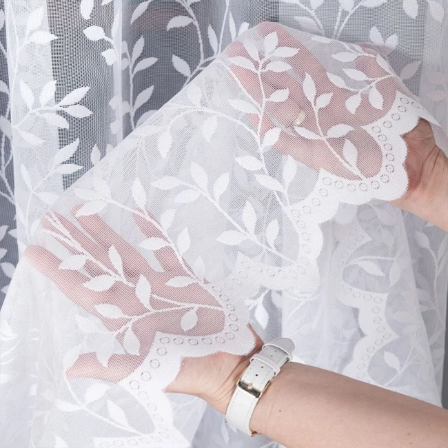 Firana żakardowa Zuzanna w kolorze białym, wysokość 250 cm, z delikatnym wzorem liści. Produkt rozłożony, uchwycony w zbliżeniu na detale, z widoczną koronkową krawędzią. Tło simple, co podkreśla fakturę materiału.