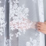 Firana żakardowa, biała, z wzorem kwiatowym, wysokość 250 cm, wisząca, ukazująca fakturę materiału. Ręka z pierścionkiem trzyma firanę, co podkreśla jej lekkość i przezroczystość. Tło proste i neutralne.